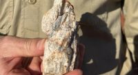 Kairos Geologist Campbell Watts holding a piece of pegmatite containing large crystals interpreted to be spodumene, discovered at ‘Lucky Sump’ during routine earth moving activities.